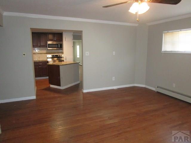 unfurnished living room featuring dark wood-style floors, baseboards, a ceiling fan, and crown molding