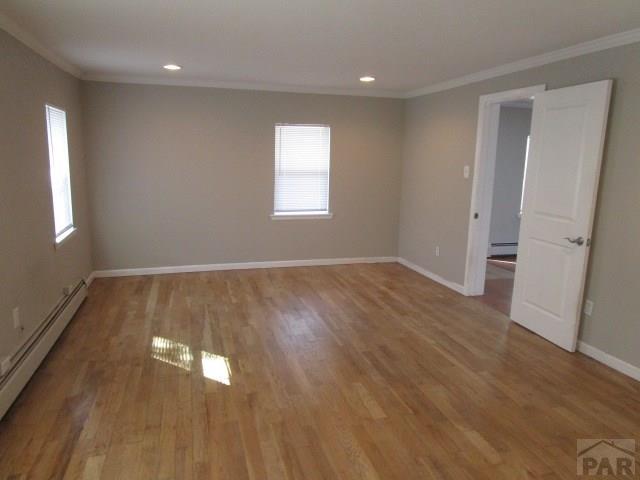 unfurnished room featuring a baseboard radiator, ornamental molding, and wood finished floors