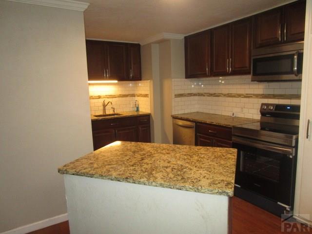 kitchen with stainless steel appliances, backsplash, a sink, light stone countertops, and baseboards