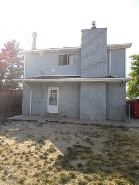 rear view of property with a chimney, fence, a lawn, and brick siding