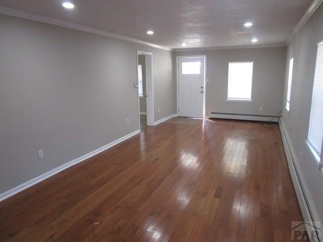 interior space featuring baseboards, a baseboard heating unit, dark wood-style flooring, and ornamental molding