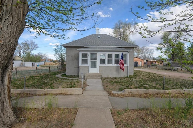 bungalow-style house featuring a shingled roof, stucco siding, fence, entry steps, and a chimney