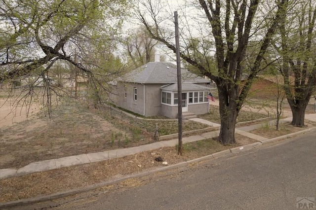 view of front of property featuring a shingled roof, a chimney, entry steps, and stucco siding