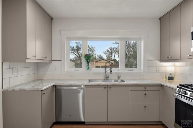 kitchen with stainless steel appliances, a sink, backsplash, and gray cabinets