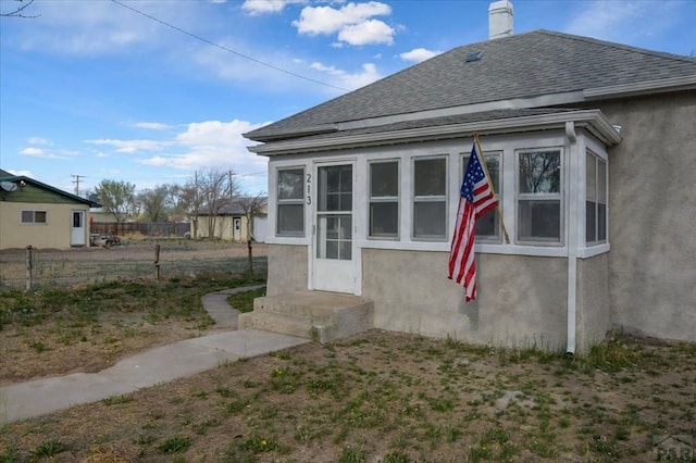 back of house featuring a shingled roof, fence, and stucco siding