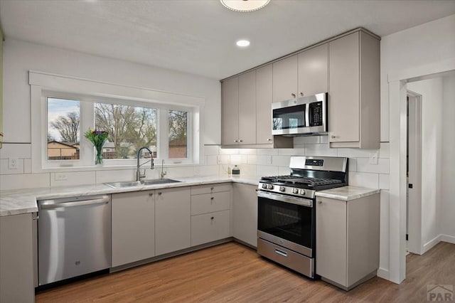 kitchen featuring appliances with stainless steel finishes, a sink, light countertops, light wood finished floors, and recessed lighting