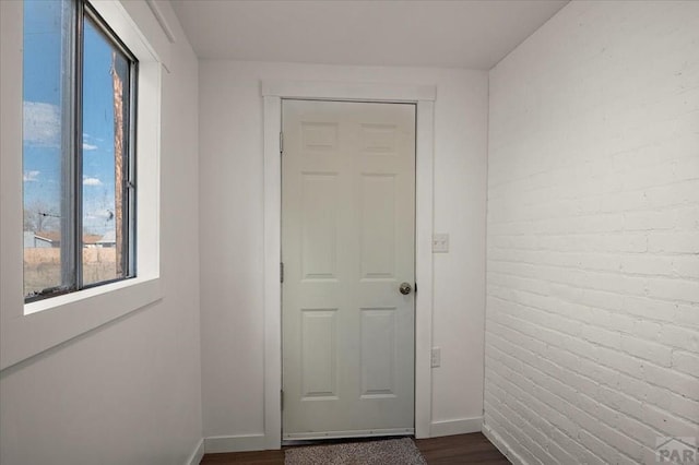 entryway with dark wood-style flooring, baseboards, and brick wall