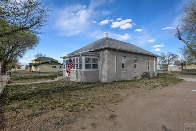 view of home's exterior featuring cooling unit, stucco siding, fence, and a chimney