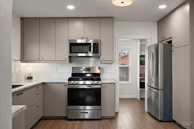 kitchen featuring appliances with stainless steel finishes, gray cabinetry, wood finished floors, backsplash, and recessed lighting