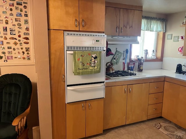 kitchen featuring under cabinet range hood, white appliances, light countertops, and a warming drawer