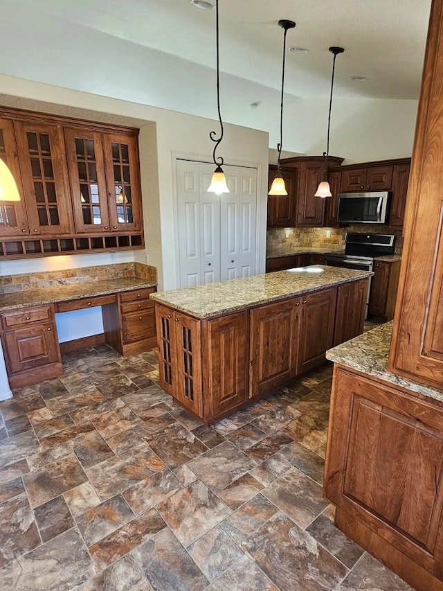 kitchen with built in desk, stainless steel appliances, tasteful backsplash, light stone counters, and a center island