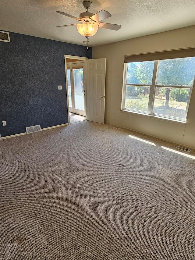 carpeted spare room featuring baseboards, visible vents, ceiling fan, and a textured ceiling