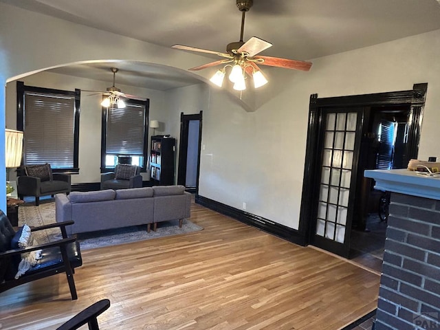 living room featuring baseboards, wood finished floors, arched walkways, and ceiling fan
