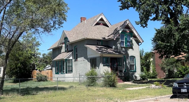 view of front facade with a chimney, a shingled roof, fence, a front yard, and stucco siding