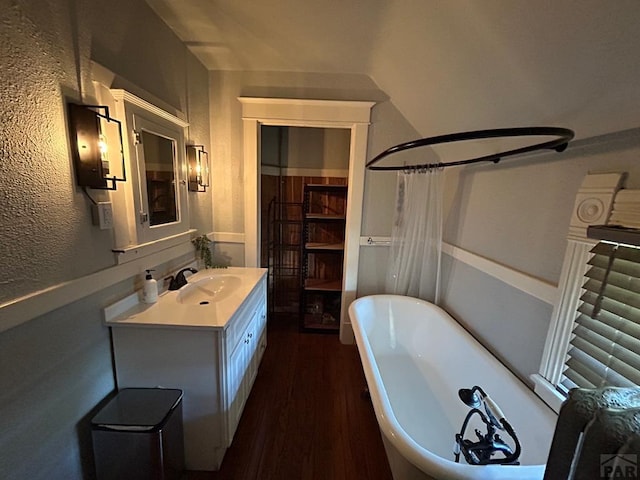 full bathroom featuring wood finished floors, vanity, a shower with curtain, a textured wall, and a freestanding bath