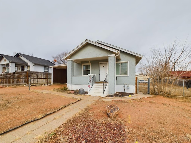 bungalow-style home featuring covered porch, fence, and stucco siding