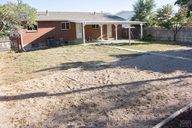 back of property featuring a fenced backyard, central AC, brick siding, a lawn, and a carport