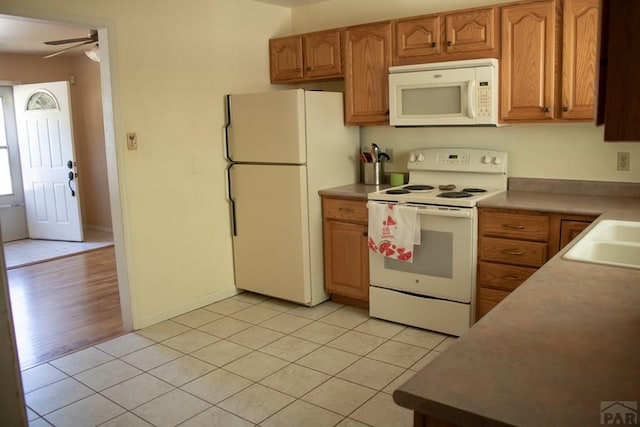 kitchen featuring light tile patterned flooring, white appliances, a sink, light countertops, and brown cabinetry