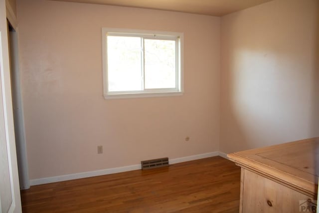 unfurnished room featuring dark wood-style floors, visible vents, and baseboards