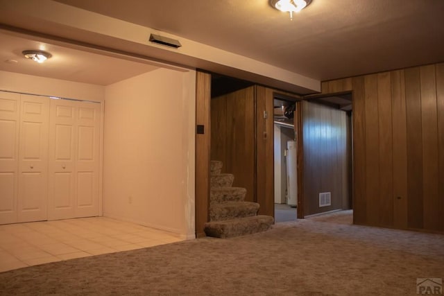 basement featuring stairs, wood walls, carpet, and visible vents