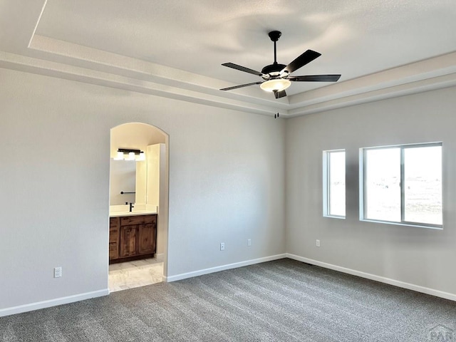 empty room featuring light carpet, baseboards, arched walkways, and a raised ceiling