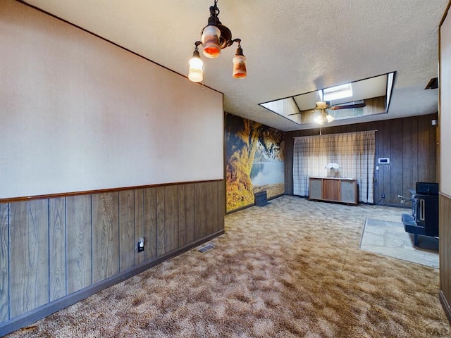 unfurnished living room with wooden walls, light colored carpet, visible vents, and a textured ceiling