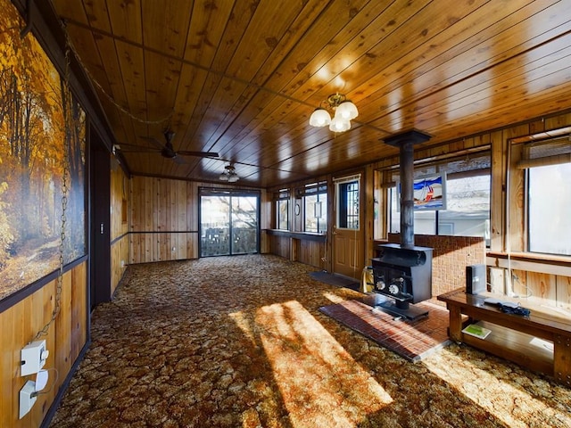 unfurnished living room featuring a wood stove, wooden ceiling, wooden walls, and carpet floors