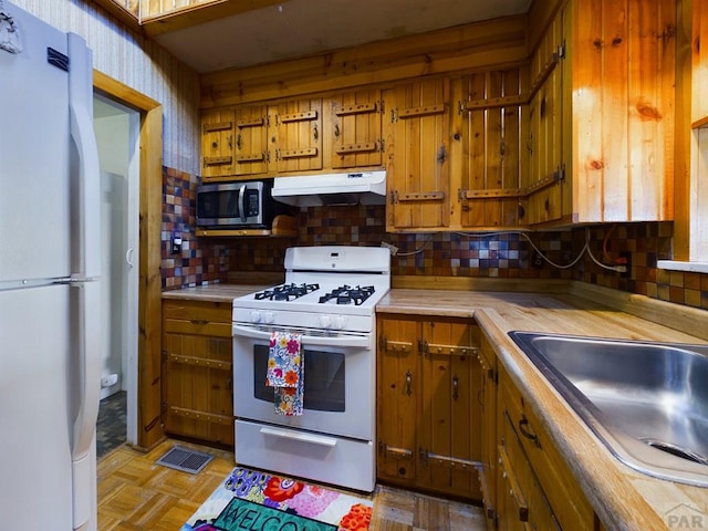 kitchen featuring brown cabinets, light countertops, a sink, white appliances, and under cabinet range hood