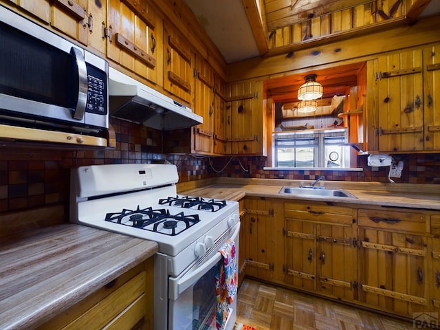 kitchen featuring white gas range oven, wood counters, stainless steel microwave, under cabinet range hood, and a sink