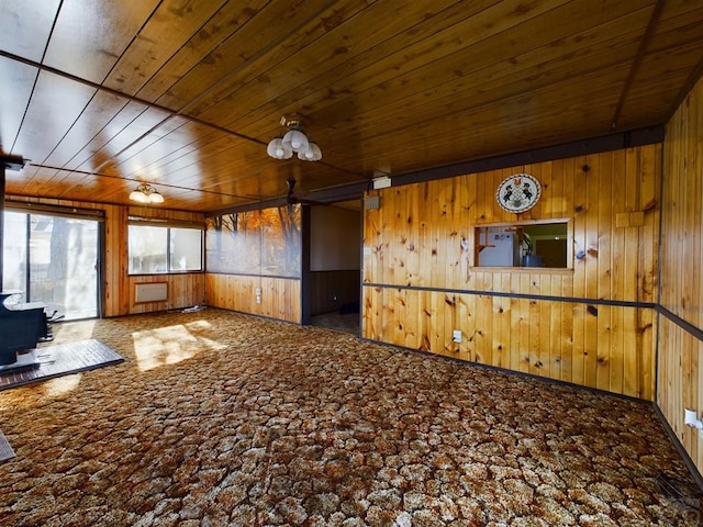 spare room featuring a wood stove, carpet flooring, wooden ceiling, and wooden walls