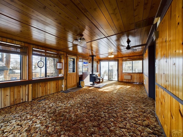 unfurnished sunroom featuring ceiling fan, wooden ceiling, and a wood stove