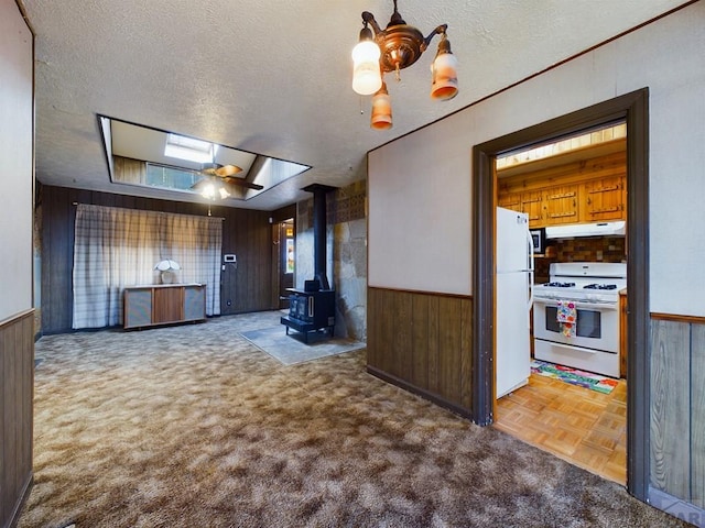 unfurnished living room featuring a skylight, a wood stove, wainscoting, wooden walls, and a textured ceiling