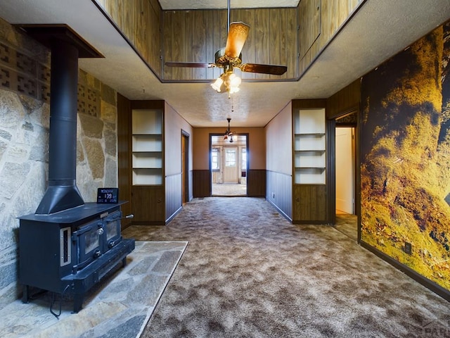 carpeted living room with a wood stove, a wainscoted wall, and ceiling fan