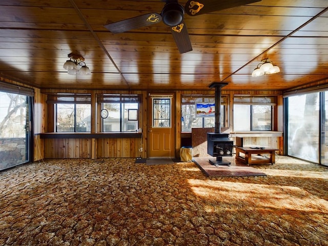 unfurnished sunroom with ceiling fan, a wealth of natural light, wooden ceiling, and a wood stove