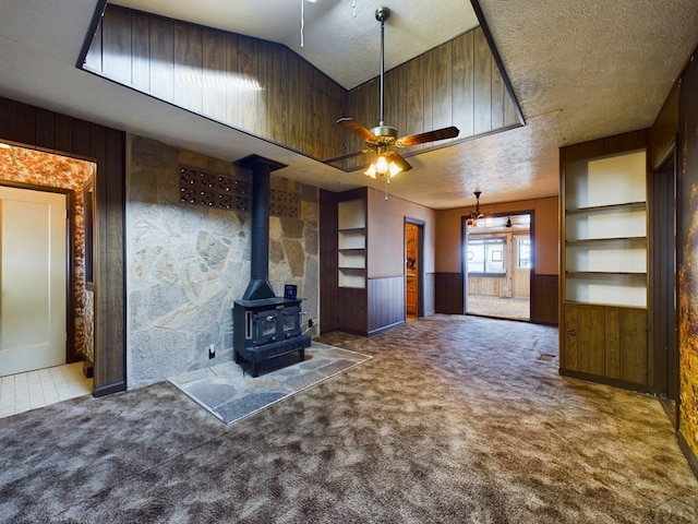 unfurnished living room with dark colored carpet, wainscoting, a wood stove, and wooden walls