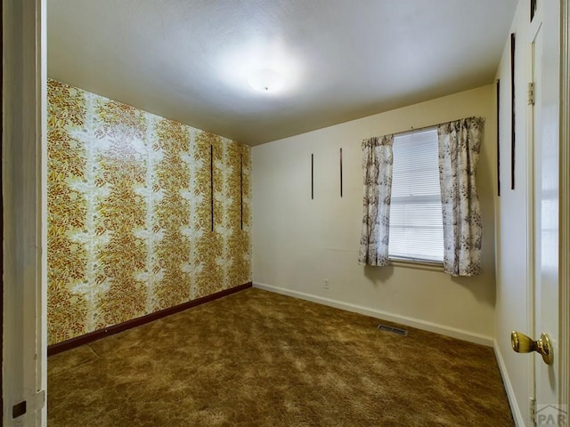 spare room with wallpapered walls, baseboards, visible vents, and dark colored carpet