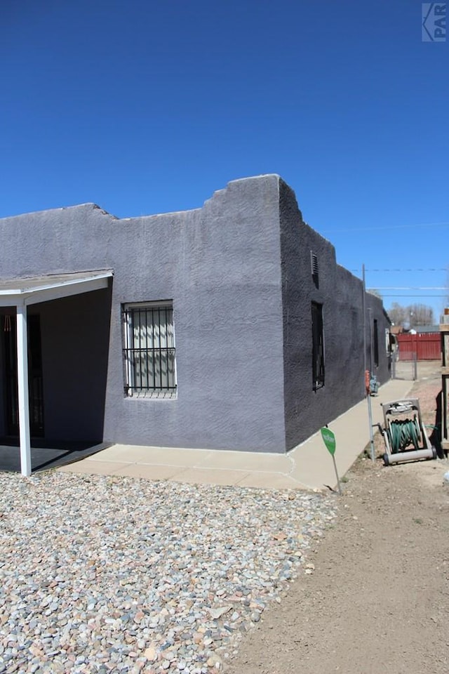 view of side of home with a patio area, fence, and stucco siding