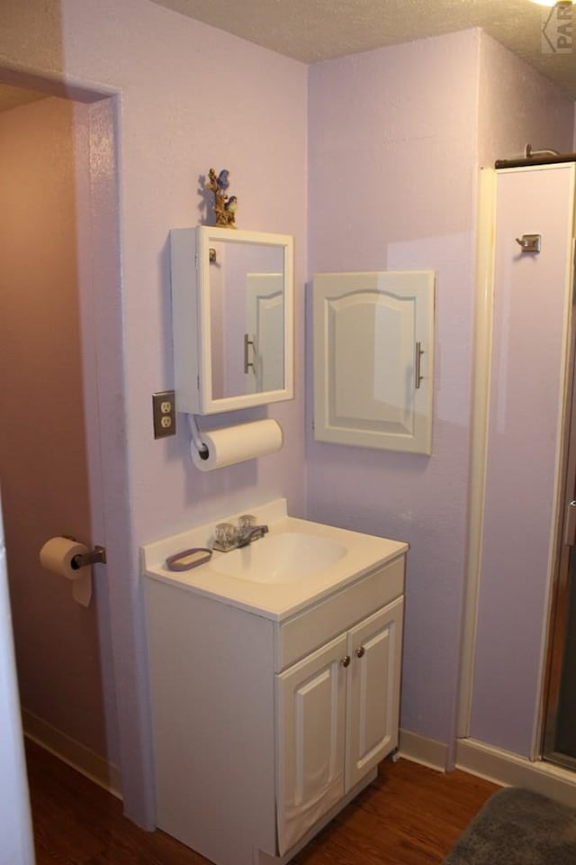 bathroom with a textured ceiling, wood finished floors, vanity, and baseboards