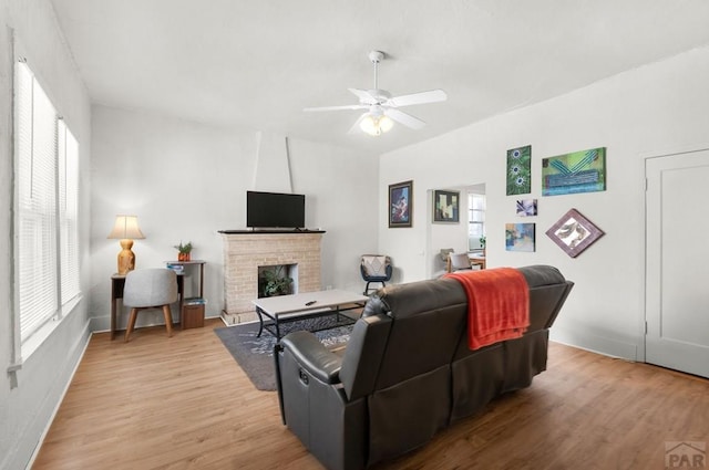 living room featuring ceiling fan, plenty of natural light, light wood-style floors, and a brick fireplace