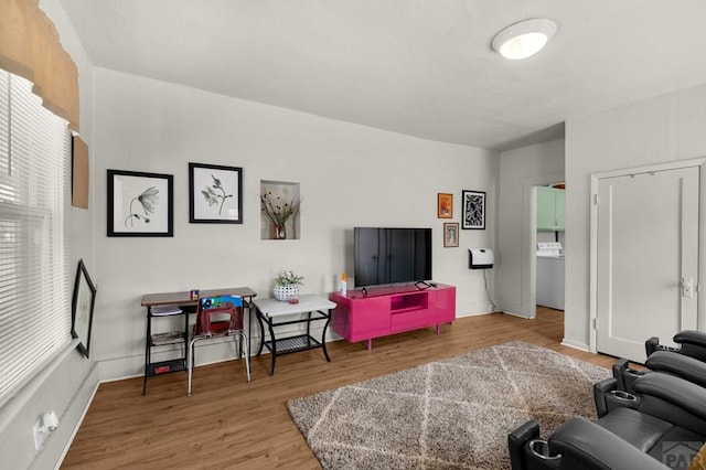 living area featuring plenty of natural light, washer / dryer, baseboards, and wood finished floors