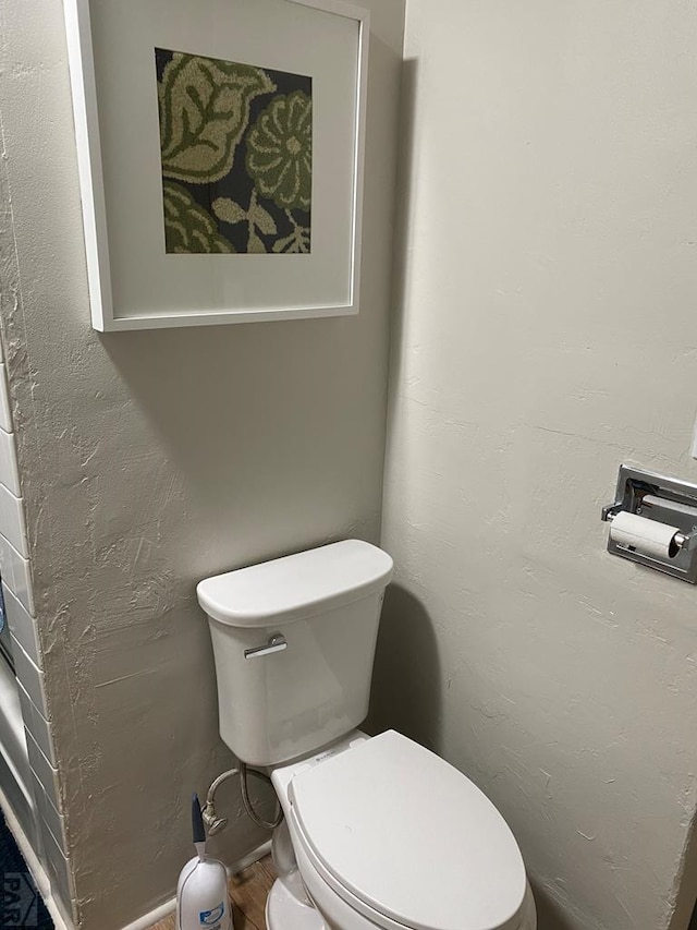 bathroom with toilet, wood finished floors, and a textured wall