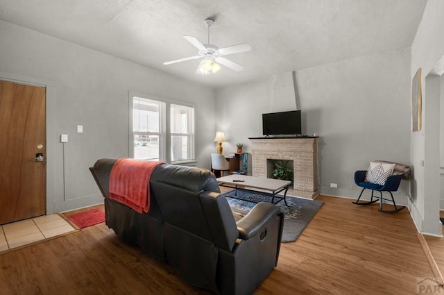 living room with wood finished floors, a fireplace, a ceiling fan, and baseboards