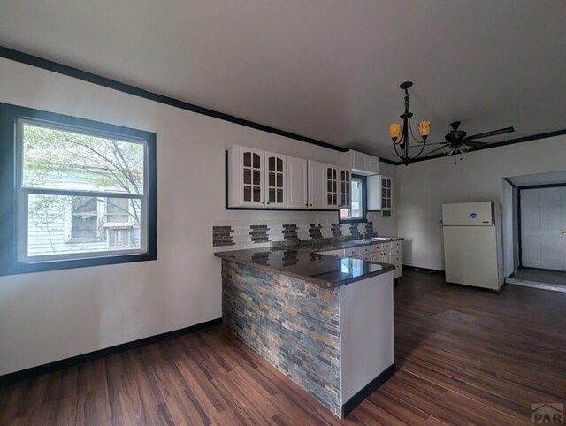 kitchen featuring white cabinetry, hanging light fixtures, freestanding refrigerator, dark countertops, and glass insert cabinets