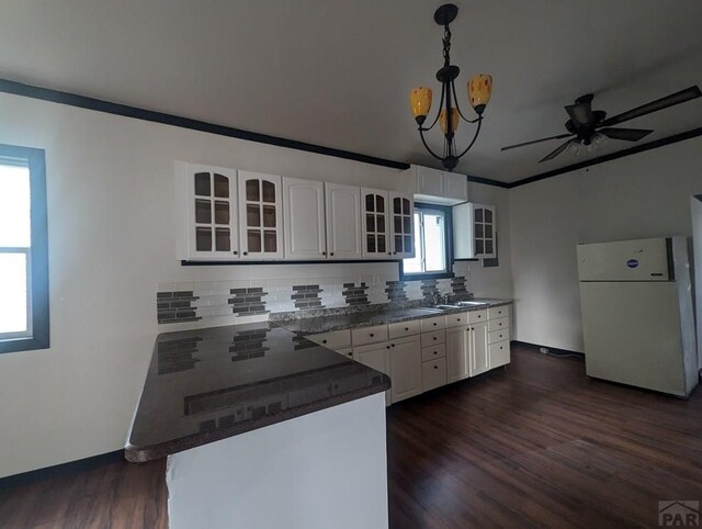 kitchen featuring a peninsula, white cabinets, freestanding refrigerator, glass insert cabinets, and pendant lighting