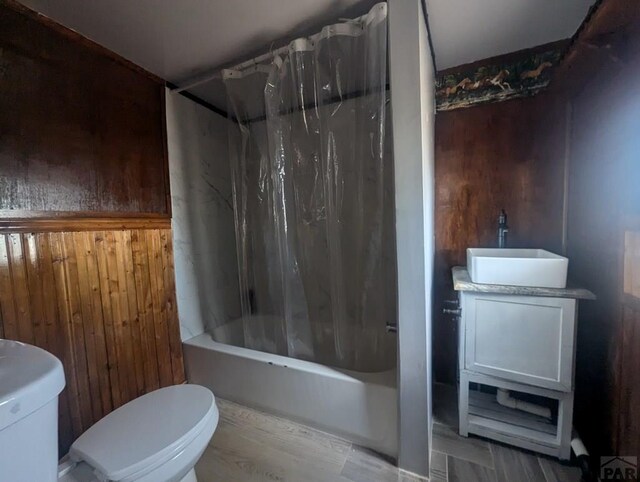 full bath featuring toilet, wooden walls, shower / tub combo with curtain, and vanity