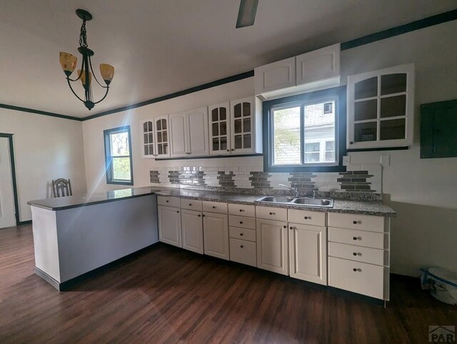 kitchen with glass insert cabinets, decorative light fixtures, a peninsula, white cabinetry, and a sink