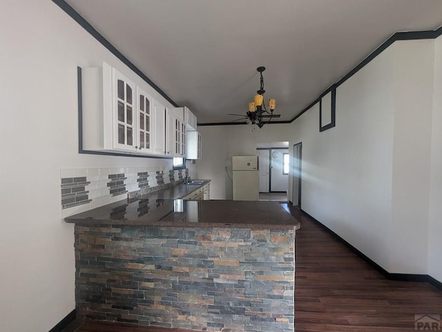 kitchen with dark countertops, glass insert cabinets, freestanding refrigerator, white cabinets, and a peninsula