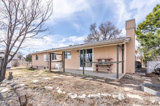 rear view of property featuring stucco siding, a patio, a chimney, and fence