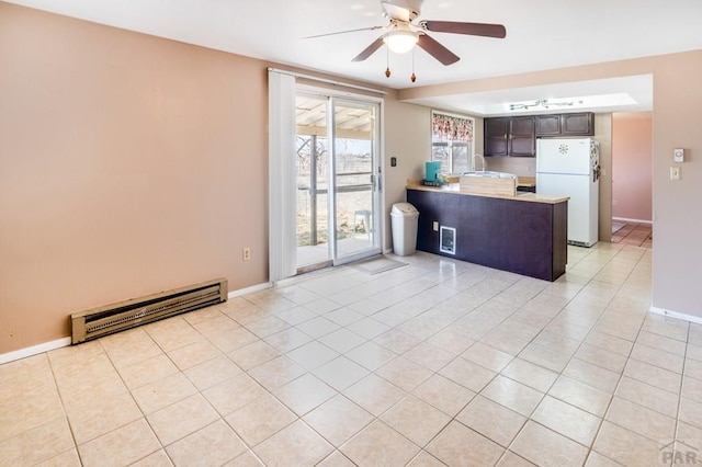 kitchen with light tile patterned floors, a ceiling fan, a peninsula, freestanding refrigerator, and baseboard heating