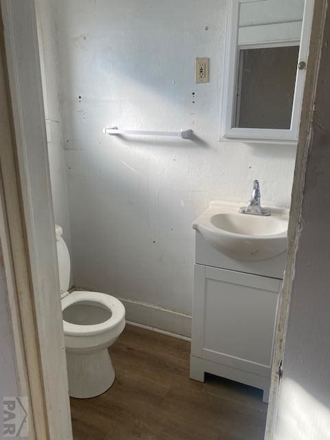 half bathroom with toilet, wood finished floors, and vanity